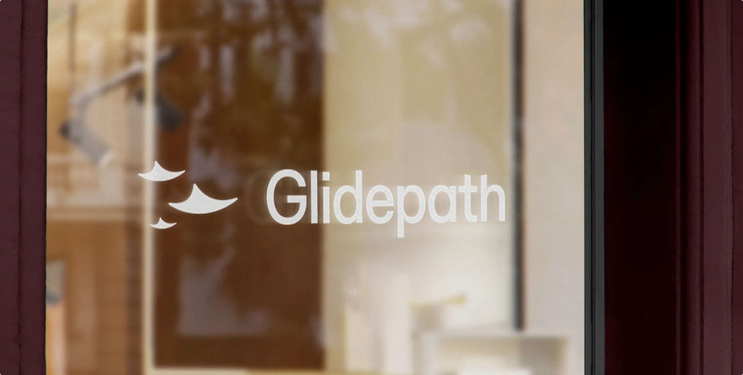 The Glidepath logomark and wordmark as a white decal on a storefront window, the interior softly out of focus behind the glass
